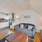 Wohnbereich mit Sofa, Tisch und Küchenzeile unter schrägen Decken.