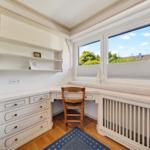 Ein Arbeitszimmer mit Schreibtisch, Stuhl und Fensterblick auf Bäume.