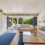 Wohnzimmer mit weißen Sofas, Glas-Tisch und Blick auf den Garten.