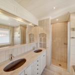 Badezimmer mit Dusche, Waschbecken und Spiegel. Wandverkleidung aus Stein.