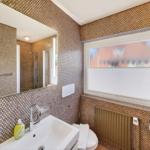 Badezimmer mit Waschbecken, Spiegel und Dusche. Wandverkleidung mit Mosaikfliesen.
