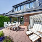 Terrasse mit Sitzgruppe, Strandkorb und Pflanzen vor einem Haus mit Dachfenstern.