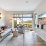 Wohnzimmer mit Sofa, Sessel und Fernseher an der Wand. Durchgang zum Garten.