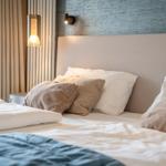 Ein Bett mit Kissen und Decke, Wandbeleuchtung und Vorhang im Hintergrund.