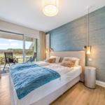 Schlafzimmer mit Bett, blauer Decke und Balkonansicht.