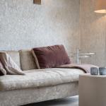 Ein Sofa mit Kissen, Beistelltisch und Stehlampe vor einer texturierten Wand.