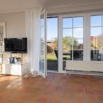 Wohnzimmer mit Terrassentür, TV und Terrasse. Terrakottafußboden und weißer Heizkörper.