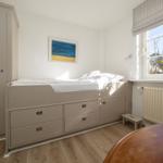 Schlafzimmer mit Bett, Schrank und Fenster mit Blumen.