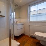 Badezimmer mit Dusche, Waschbecken und Toilette. Fenster mit Jalousie und Heizkörper.