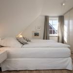 Schlafzimmer mit Doppelbett, Nachttisch, Gardinen und Kleiderschrank.