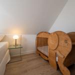 Schlafzimmer mit Babybett und Nachttisch unter schrägem Dach