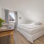 Schlafzimmer mit Dachschrägen, Bett, Tisch und Blumen.