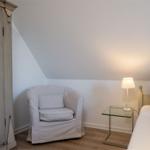 Schlafzimmer mit Bett, Sessel und Nachttisch unter schrägem Dach.