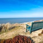 A green wooden bench on a dune with a view of the sea and sky.
