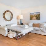 Bedroom with sofa, bed, and wooden floor. Wall art and mirror visible.