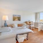 A bedroom with a white bed, sofa, table, and chairs. Large windows with a view of a meadow.