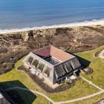 House with thatched roof is directly on the beach. Green lawns and walking paths surround the property.