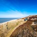 A green chair on a dune with a view of the sea and blue sky.