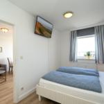 Schlafzimmer mit Bett, TV und Blick auf Balkon. Durchgang in Wohnbereich mit Sofa.