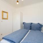 Schlafzimmer mit Doppelbett, blauer Bettwäsche, weißem Kleiderschrank und goldgerahmtem Spiegel an der Wand.