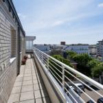 Terrasse mit weißer Brüstung und Blick auf Gebäude und Bäume.