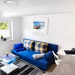 Ein Wohnbereich mit blauem Sofa, Glas-Tisch und Wandbild.
