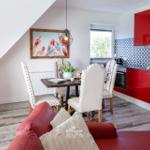 Essbereich mit rotem Sofa, Esstisch und roter Küche unter Dachschrägen.