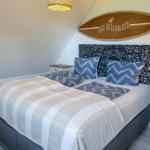 Schlafzimmer mit Bett, Nachttischen und Surfbrett an der Wand.