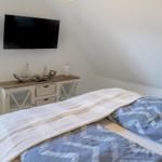 Schlafzimmer mit Dachschräge, Bett mit gemustertem Bettbezug, TV und Schrank.