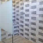 Dusche mit Glaswand und gemusterten Fliesen