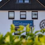Weißes Haus mit dunklem Dach, Schild und Wanduhr