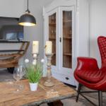 Ein Wohnzimmer mit rotem Ledersessel, Holztisch und Fernseher auf rustikalem Gestell.
