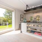 Küche mit Blick auf Garten, weiße Schränke, offene Regale und drei Bogenfenster.