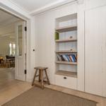 Eingangsbereich mit Bücherregal und Holzstuhl. Durchgang zu Wohnzimmer mit Tisch und Stühlen.