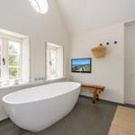 Bad mit freistehender Badewanne, Fenstern und Fernseher an der Wand.