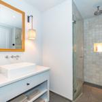 Badezimmer mit Dusche und Waschbecken. Glasdusche, Spiegel und Schrank.