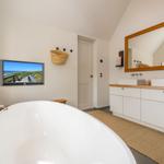 Badezimmer mit freistehender Badewanne, Doppelwaschbecken und Fernseher an der Wand.