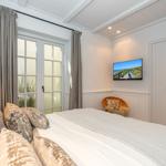Schlafzimmer mit Bett, TV und Fenster. Wand und Decke weiß. Vorhänge grau.