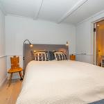 Schlafzimmer mit Bett, zwei Nachttischen und Wandbild. Hölzerne Bodenplanken und weiße Wände.