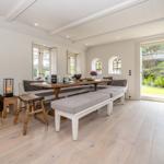 Esszimmer mit Holztisch, Sitzbänken und großem Fenster zur Gartenansicht.