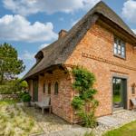 Rotes Backsteinhaus mit Strohdach, Gartenbereich und Holzbänken.