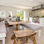 Großer Essbereich mit Holztisch, Bank und Sofa. Küche mit Arbeitsplatte und Fenstern.