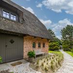 Haus mit Strohdach, Backsteinfassade und Holzbank im Garten.