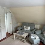 Wohnzimmer mit grauem Sofa, Sessel und Couchtisch unter schrägen Dachschrägen.