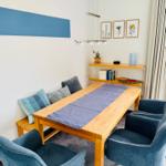 Esszimmer mit Holztisch, blauen Stühlen und Wanddekoration.