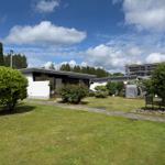 Moderne Villa mit Garten, Rasen und Blumen. Hintergrund: Baustelle und Bäume.