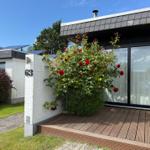 Haus mit roter Rosenhecke, Holzterrasse und weißem Mauerabschnitt mit Hausnummer 63.