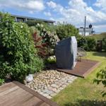 Garten mit Holzterrasse, Beete mit Blumen und einem gedeckten Grill.