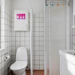 Bathroom with toilet, shower, and sink. White tiles and storage shelves.