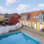 Pool area with yellow houses and white fence. Outdoor furniture and red roofs.